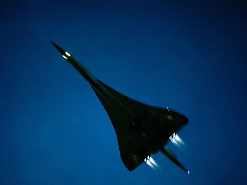 A supersonic airliner overhead at dusk, nose raised